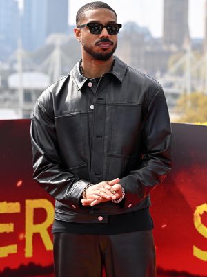 Michael B. Jordan wearing a black leather jacket and pants by GapStudio, standing in front of a red and yellow backdrop with the London skyline behind him