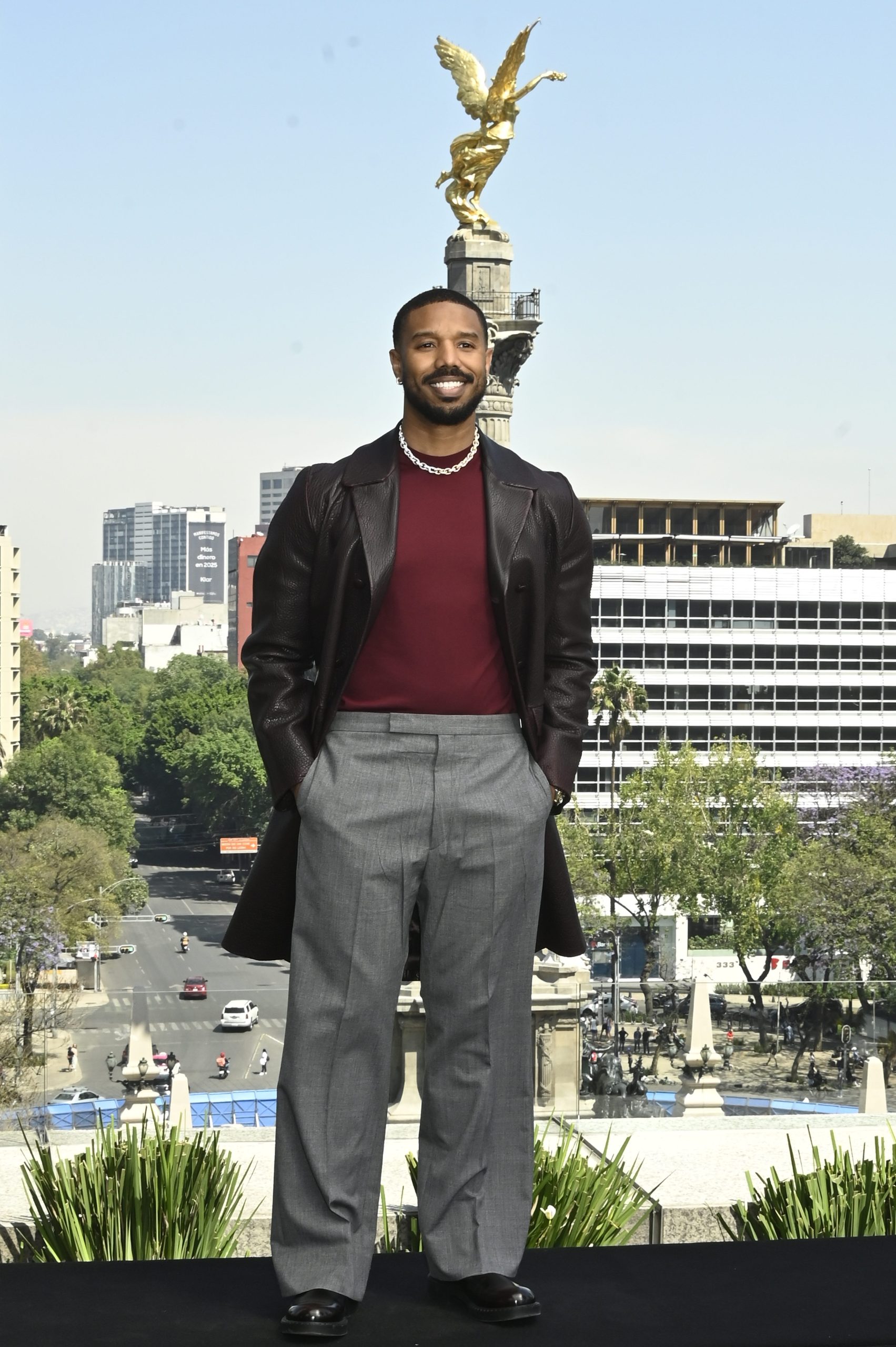 Michael B. Jordan wearing a brown leather coat over a burgundy knit and gray trousers at the Sinner premiere