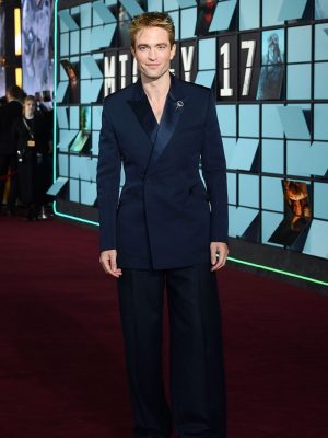 Robert Pattinson on the red carpet in a navy silk Dior suit with wide trousers and black satin boots at the "Mickey 17" premiere.