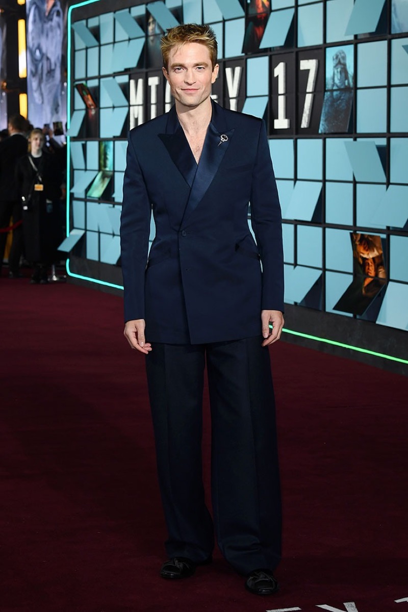 Robert Pattinson on the red carpet in a navy silk Dior suit with wide trousers and black satin boots at the "Mickey 17" premiere.