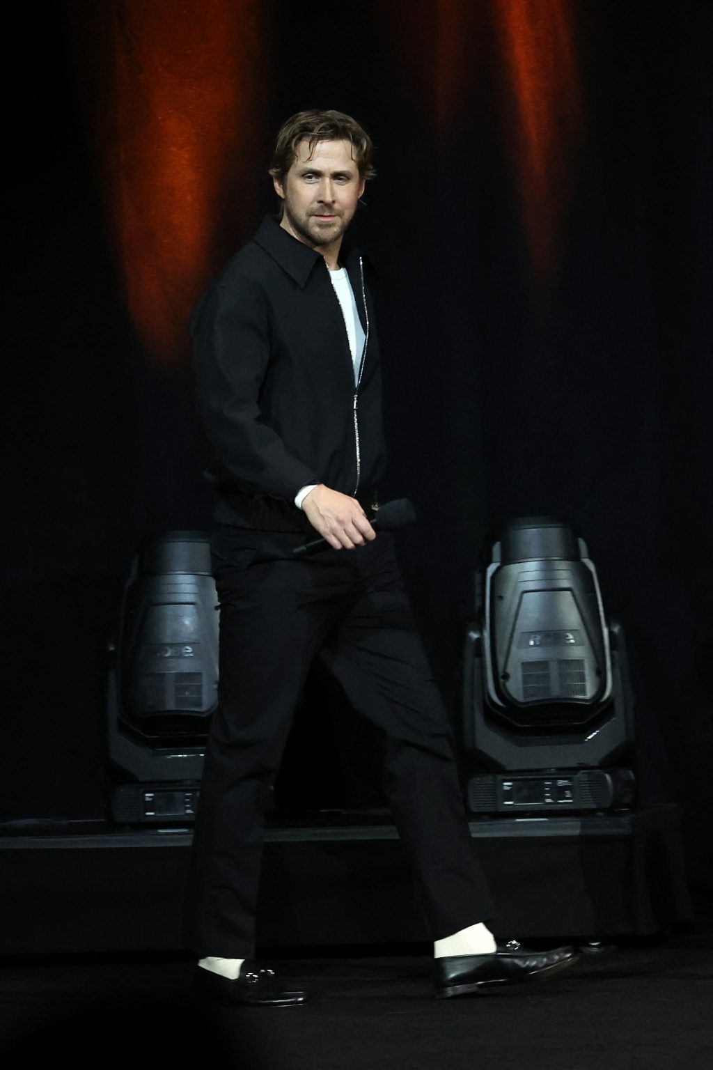 Ryan Gosling walks on stage in an all-black Gucci outfit featuring a zip-up jacket, trousers, and black Horsebit loafers with white socks at CinemaCon 2025.