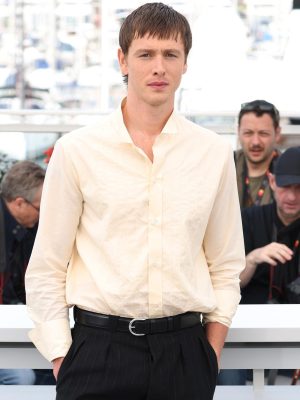 Harris Dickinson posing in front of photographers at the Cannes Film Festival in a cream Prada shirt and black trousers.