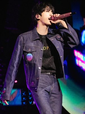Jin of BTS performing in a dark denim Gucci outfit, holding a pink microphone during Coldplay’s Music Of The Spheres concert.