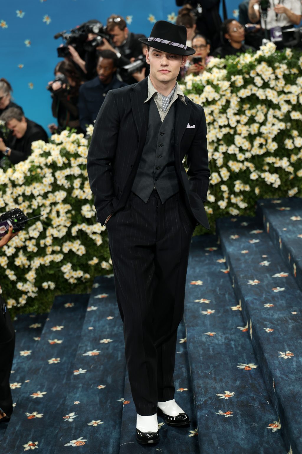 Louis Partridge in a black pinstripe Prada suit with a blue ascot and lilac pocket square at the 2025 Met Gala.