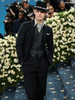Louis Partridge in a black pinstripe suit with a blue ascot and lilac pocket square at the Met Gala.